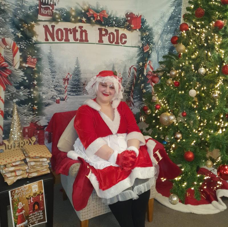 Woman dressed as Mrs Claus next to a Christmas Tree
